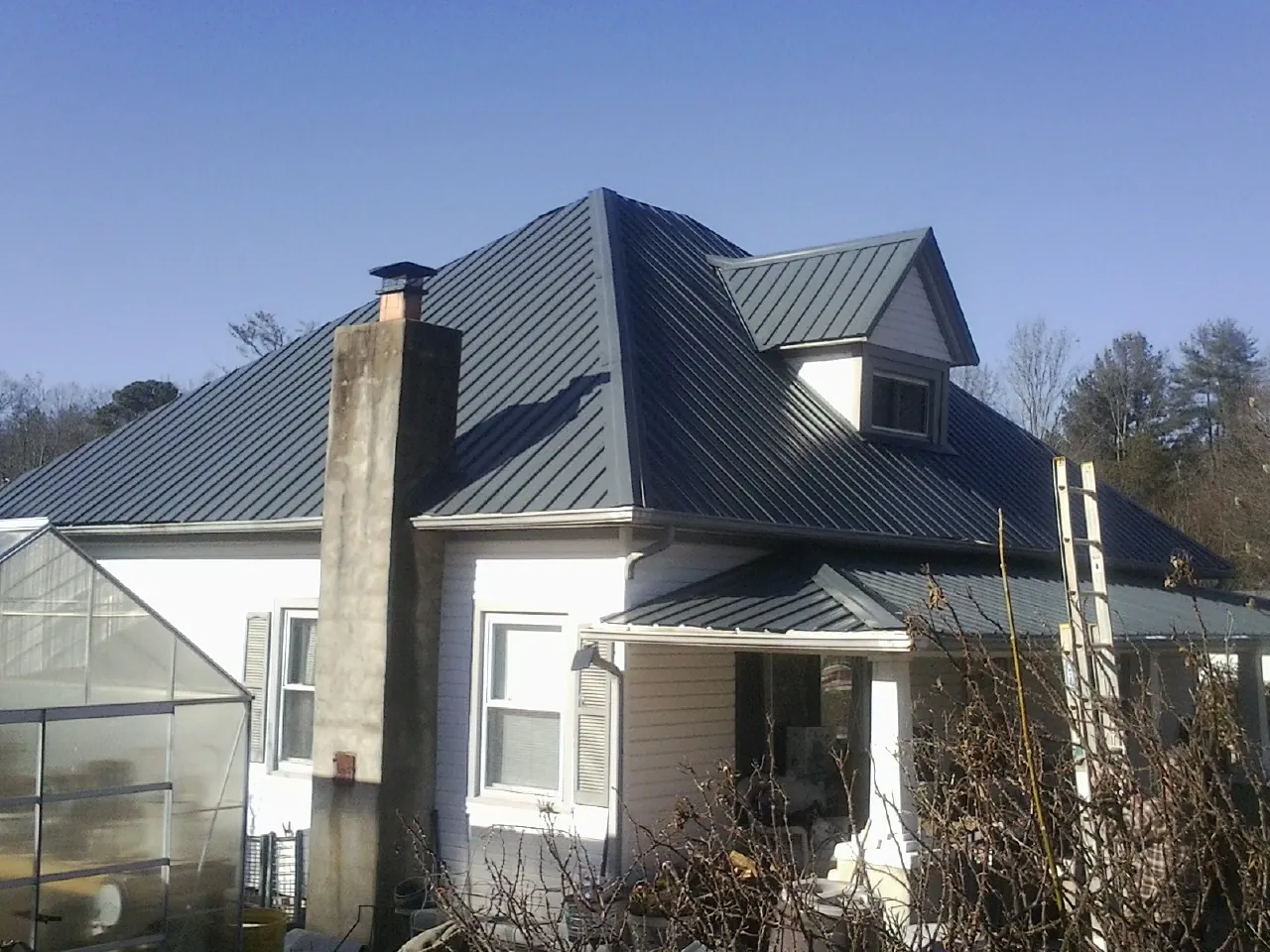 Dark blue standing seam metal roof on a white farmhouse with dormer — Slate & Tile Roof Repair by Roofing Brothers in Tuskegee Institute