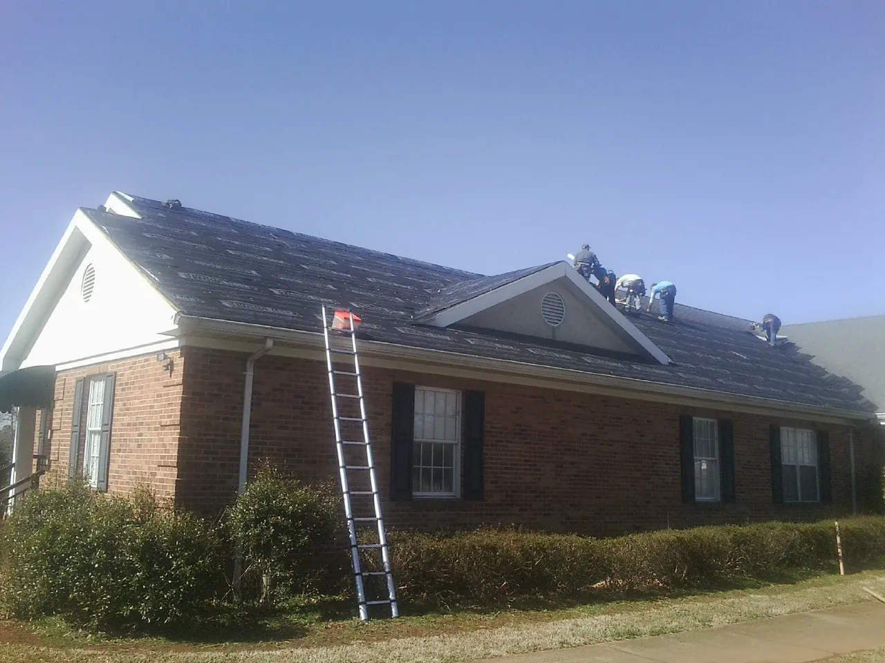 Crew tearing shingles off a brick ranch roof with a ladder set — Metal Roof Repair work by our crew in Tuskegee Institute