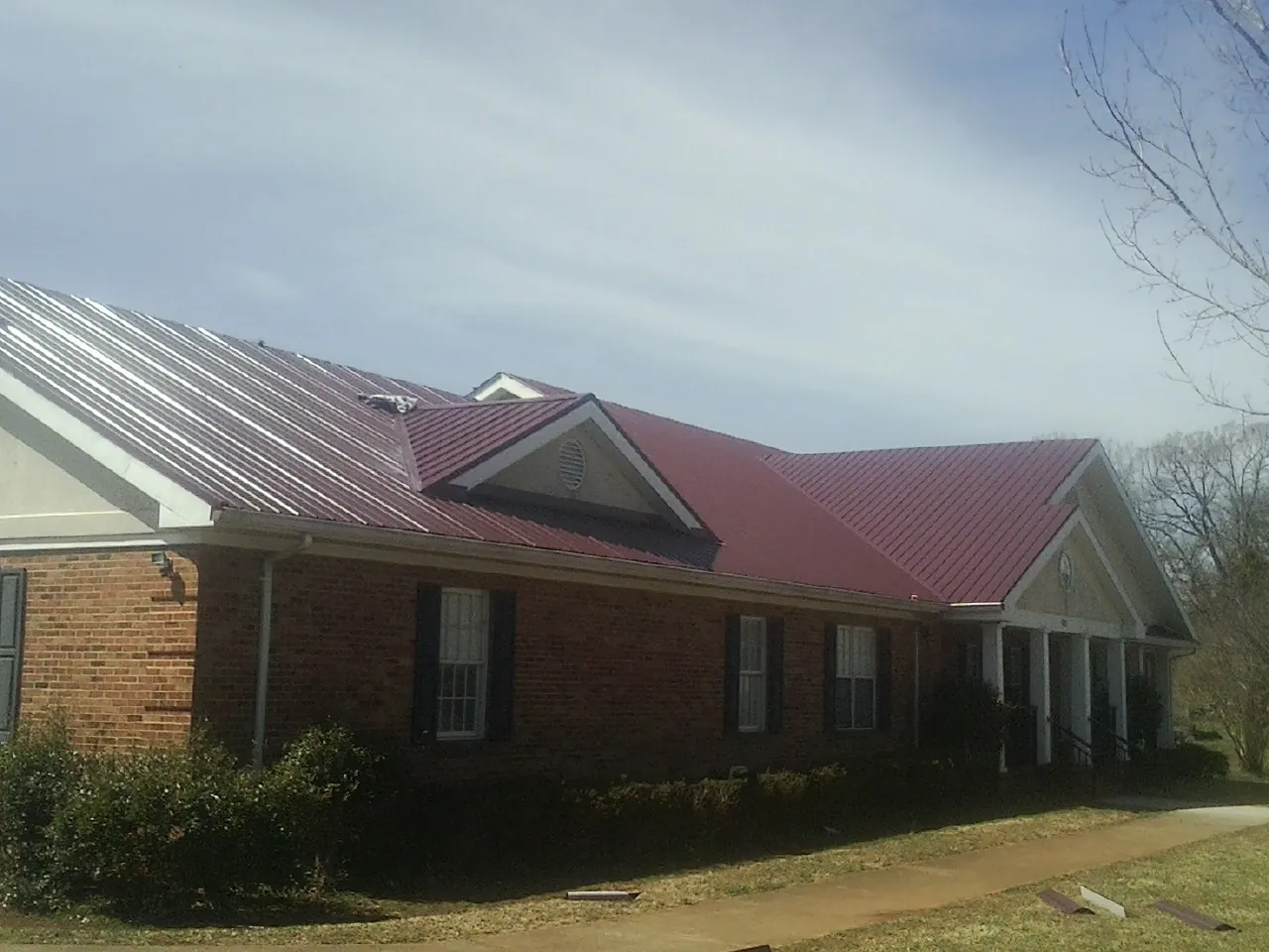 Red metal roof with gabled entries on a long brick building, from a Hail Damage Roof Repair job in Tuskegee Institute