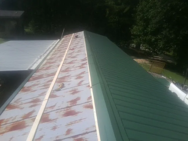 Old rusted panels beside newly installed green metal roofing — Wind Damage Roof Repair by Roofing Brothers in Tuskegee Institute