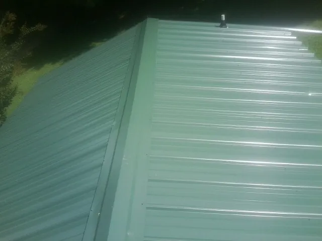 New green metal panels meeting at the ridge of a roof — Flat Roof Repair work by our crew in Tuskegee Institute