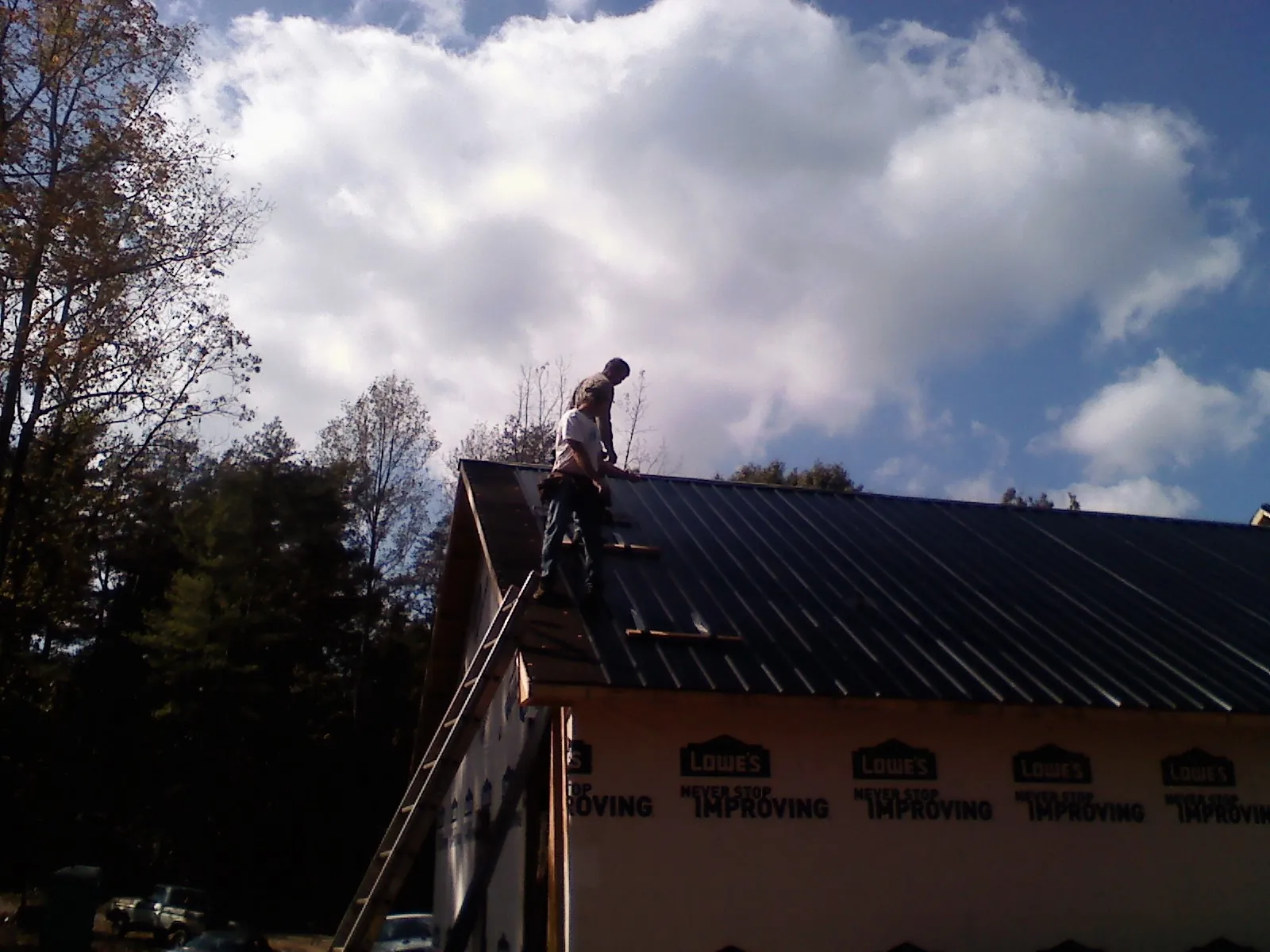 Roofer fastening dark metal panels high against a cloudy sky, from a Roof Inspection job in Tuskegee Institute