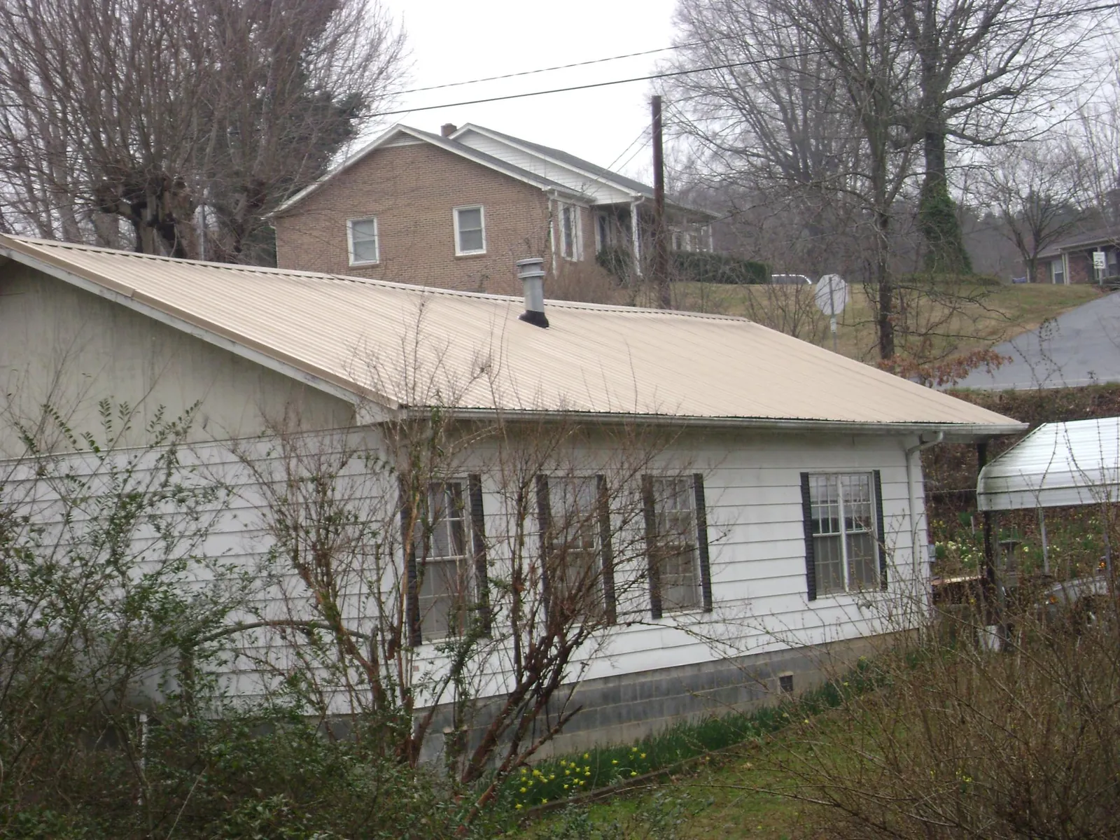 Tan metal roof on a white sided house set into a hillside — Commercial Roofing by Roofing Brothers in Tuskegee Institute